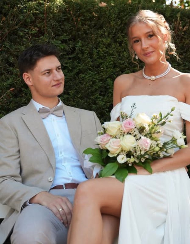 Brautpaar sitzt mit Blumenstrauß auf einer Bank